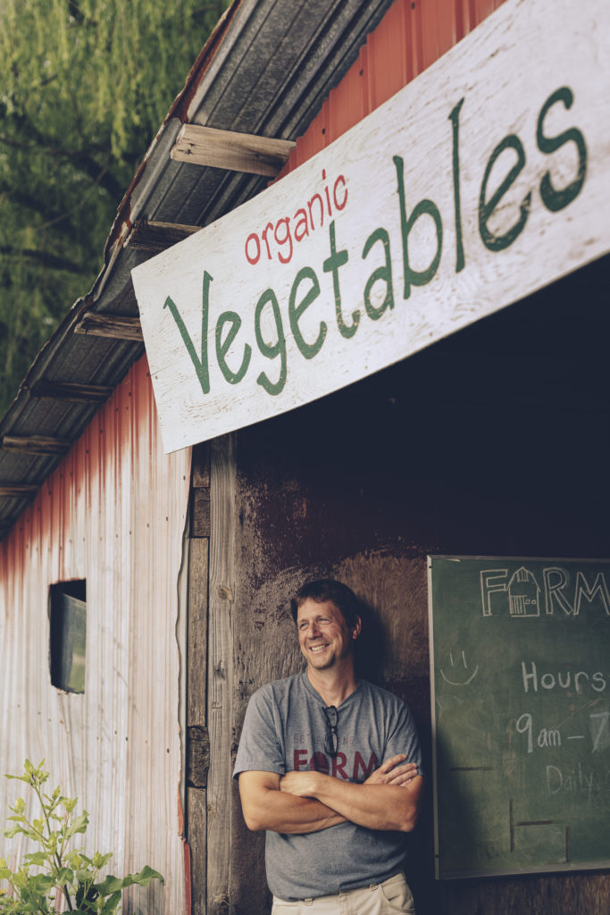 mike standing under the organic vegetables sign in his red barn